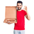 © Krakenimages.com - Young handsome man with beard holding delivery cardoboard with italian pizza doing ok sign with fingers, smiling friendly gesturing excellent symbol