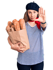 Sticker - Young beautiful blonde woman wearing french beret holding bag with bread with open hand doing stop sign with serious and confident expression, defense gesture