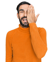 Poster - Young hispanic man wearing casual clothes covering one eye with hand, confident smile on face and surprise emotion.