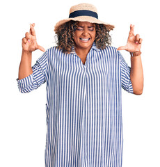 Wall Mural - Young african american plus size woman wearing summer hat gesturing finger crossed smiling with hope and eyes closed. luck and superstitious concept.