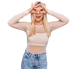 Wall Mural - Young blonde woman wearing casual clothes doing ok gesture like binoculars sticking tongue out, eyes looking through fingers. crazy expression.