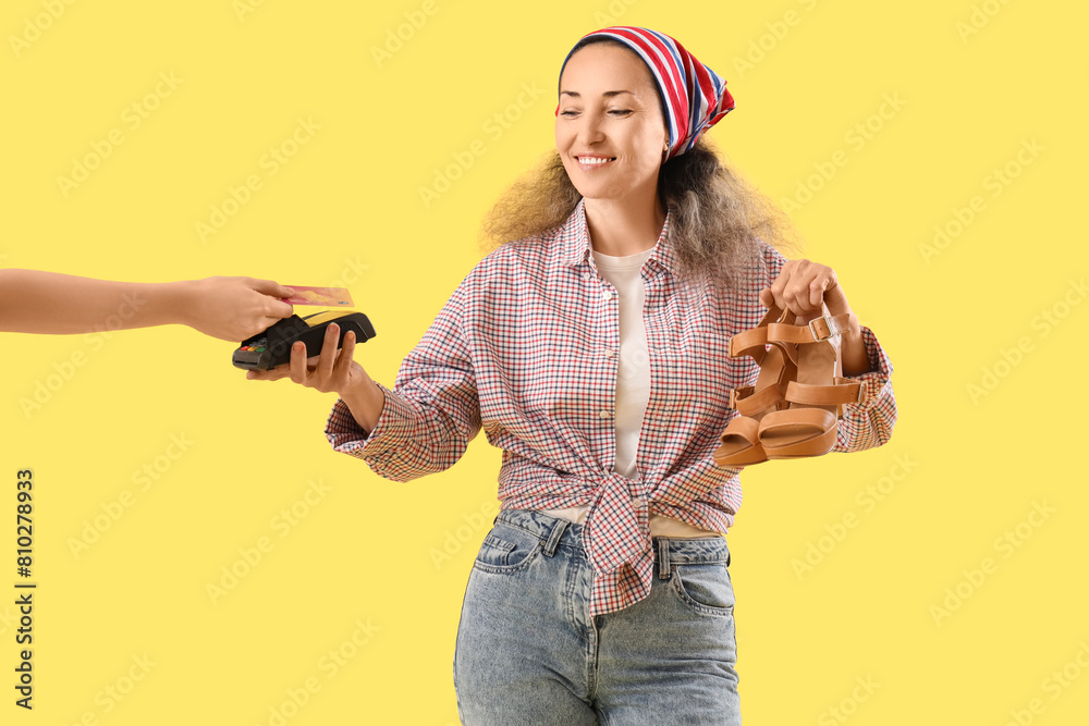 Female shoemaker taking payment for repaired shoes on yellow background