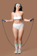 Poster - Beautiful young body positive woman in stylish underwear with jumping rope on brown background