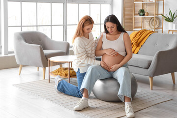 Canvas Print - Young pregnant woman on fitball with doula at home