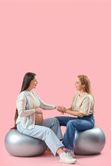 Sticker - Mature doula with pregnant woman on fitballs holding hands against pink background