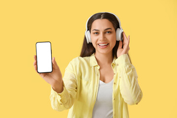 Canvas Print - Beautiful young happy woman in headphones listening music on yellow background