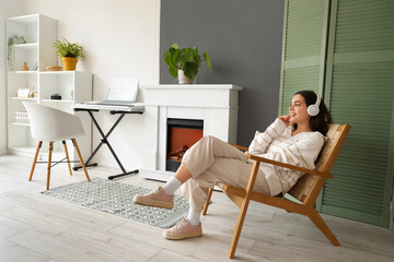 Wall Mural - Beautiful young woman in headphones sitting on chair and listening music at home