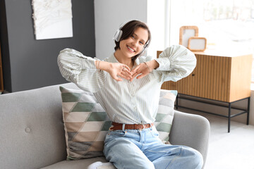 Poster - Beautiful young woman in headphones listening to music on sofa at home