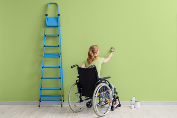 Poster - Young woman in wheelchair with brush painting green wall, back view