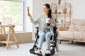 Wall Mural - Young Asian woman in wheelchair with paint brush and can during repair at home