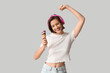 Happy young woman in headphones with sweet ice-cream in waffle cone on grey background
