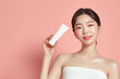 © fahrwasser - Beautiful perfect skin Korean woman holding a tube of face cream for a commercial on light pastel background, cosmetic mock up