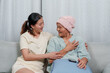 © Ekkasit A Siam - Caring Asian young adult, comforting older woman in pale blue attire, pink beanie, affection, and positive encouragement visible. mother sick and daughter take care of