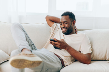 African American man sitting on a black sofa, happily using his smartphone to chat and connect with friends via social media He is relaxed and confident, enjoying his leisure time at home The modern