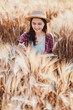 © Satori Studio - Joyful young woman with a straw hat writes in her notebook, immersed in the golden hues of a wheat field.