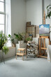 Streamlined creative artist workplace with easel, oil artwork painted on canvas. Painter home art studio decorated with multiple green fresh plants, potted flowers. Inspiring bright work environment