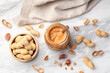Peanut butter in jar and roasted peanuts in wood bowl on marble table