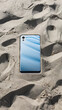 A phone is sitting in the sand with a blue background.
