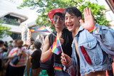 Fototapeta  - LGBTQ men have fun celebrating their pride with flags at the annual Pride Parade, waving rainbow flags in hands, celebrate LGBTQ Pride Month Parade, smiling and looking at camera