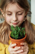 A child, dressed in a vibrant yellow sweater, delicately holds a terracotta pot with a green plant.