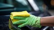 A worker's hand cleaning a car with a microfiber cloth and sponge.