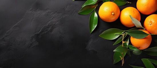 Poster - Top view of a flat lay fruit composition featuring an orange or tangerine with leaves placed on a black stone background The image provides copy space for text or other elements