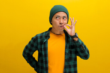 Young Asian man, dressed in a beanie hat and casual shirt, zips his lips in a promise to keep a secret, symbolically sealing his lips as if on a lock, while standing against a yellow background