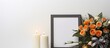 Indoors there is a photo frame adorned with a black ribbon a burning candle placed on a light grey table and a wreath of plastic flowers positioned near the wall This setup provides a suitable backgr