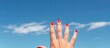 A woman s hand adorned with red painted nails and a black ring on the pinky finger reaches out into the vast expanse of a blue sky creating a beautiful copy space image 200 characters