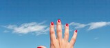 Fototapeta Dinusie - A woman s hand adorned with red painted nails and a black ring on the pinky finger reaches out into the vast expanse of a blue sky creating a beautiful copy space image 200 characters