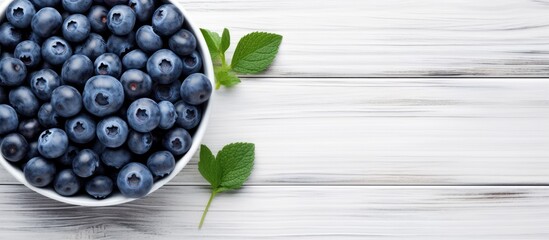 Poster - A summery image of ripe blueberries arranged in a blue bowl on a white wooden surface seen from above The flat overhead perspective leaves plenty of empty space for text or other elements