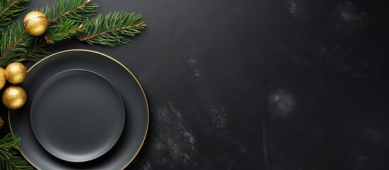 Top view of a Christmas table setting on a black stone background The elegant arrangement includes an empty black ceramic plate a fir tree branch and gold accessories The image has copy space availab