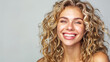 Beautiful blonde woman with curly hair is smiling on a gray backdrop.