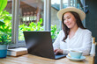Portrait image of a young woman with hat working on laptop computer in cafe