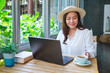 Portrait image of a young woman with hat working on laptop computer while drinking coffee in cafe