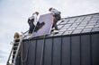 Electricians installing solar panel system on roof of house. Men workers in helmets carrying photovoltaic solar module outdoors. Concept of alternative and renewable energy.