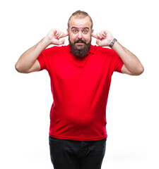 Sticker - Young caucasian hipster man wearing red shirt over isolated background covering ears with fingers with annoyed expression for the noise of loud music. Deaf concept.