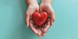 Woman hands holding red heart on solid light blue background. Health care, organ donation, cardiac health problems.