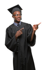 Wall Mural - Young graduated african american man over isolated background smiling and looking at the camera pointing with two hands and fingers to the side.