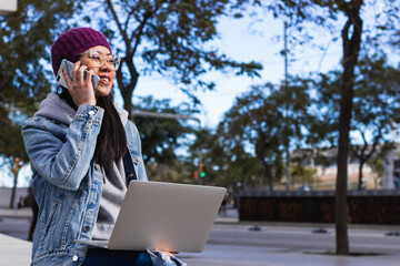 Young asian student working using laptop sitting on the bench in the city