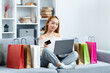 Happy Young Woman Online Shopping With Laptop And Credit Card, Surrounded By Colorful Shopping Bags On A Cozy Sofa, Modern Lifestyle And E-Commerce Concept