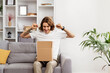Happy Young Man Unboxing In Living Room, Surprised And Triumphantly Raising Fists, Modern Cozy Home Decor Background, Excitement Of New Purchase