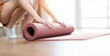 Close-up of attractive young woman folding yoga mat after working out at home in living room.
