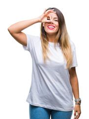 Wall Mural - Young beautiful woman casual white t-shirt over isolated background doing ok gesture with hand smiling, eye looking through fingers with happy face.