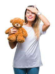 Wall Mural - Young beautiful woman holding teddy bear plush over isolated background stressed with hand on head, shocked with shame and surprise face, angry and frustrated. Fear and upset for mistake.