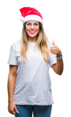 Wall Mural - Young beautiful woman wearing christmas hat over isolated background doing happy thumbs up gesture with hand. Approving expression looking at the camera with showing success.