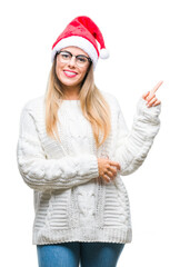 Poster - Young beautiful woman wearing christmas hat over isolated background with a big smile on face, pointing with hand and finger to the side looking at the camera.