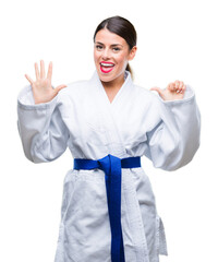 Poster - Young beautiful woman wearing karate kimono uniform over isolated background showing and pointing up with fingers number six while smiling confident and happy.