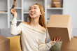 Happy Young Woman Unpacking Boxes In New Home, Holding Credit Card Excited About Online Shopping, Relocating Concept