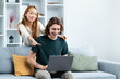 Couple Using Laptop On Sofa At Home: A young couple, woman and man, happily engaged with a laptop on a cozy couch in a modern living room.